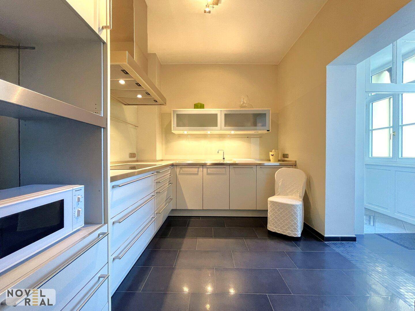Moderne Küche mit weißen Schränken, dunklem Fliesenboden und Mikrowelle.