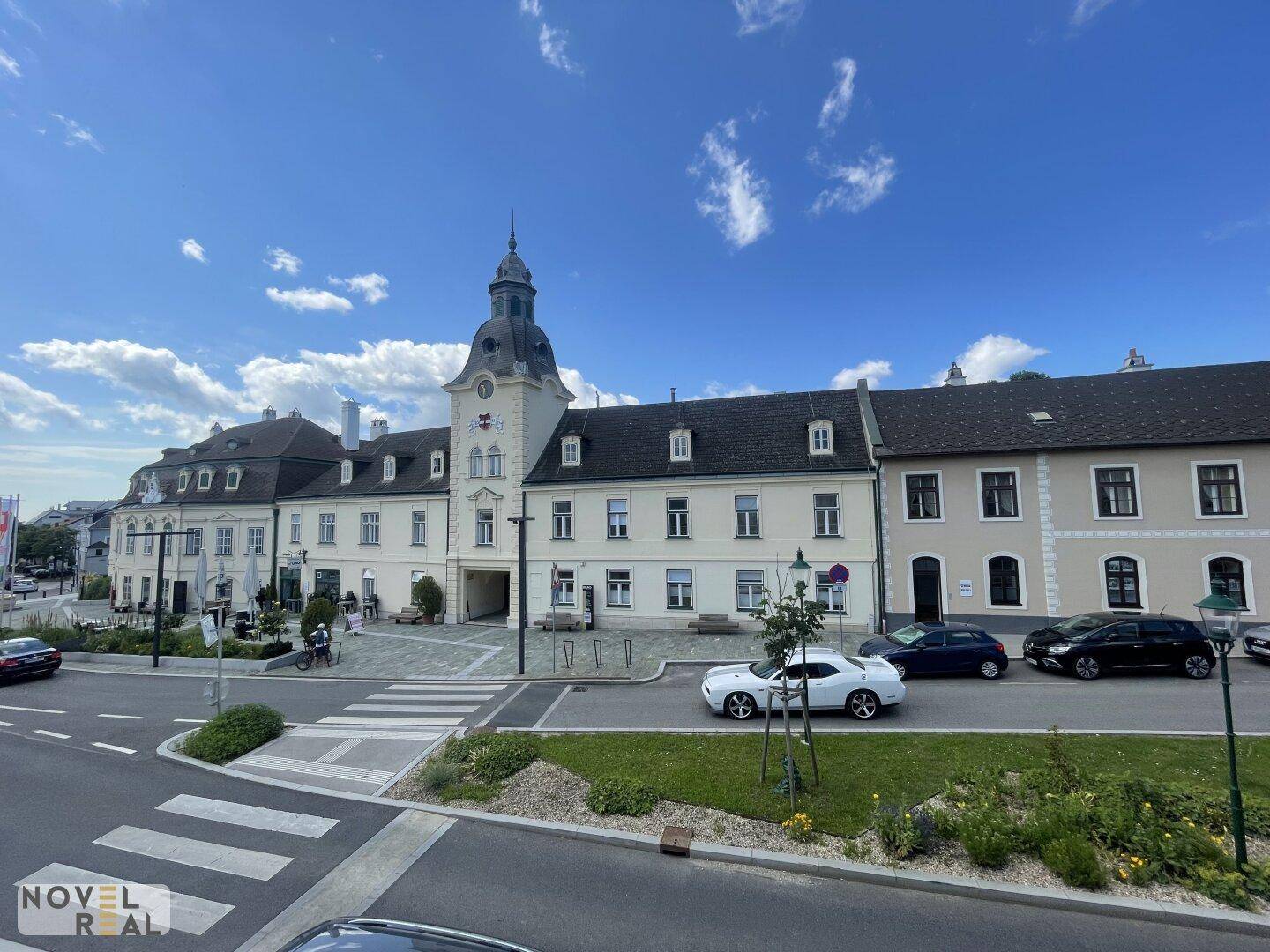 Historisches Gebäudeensemble mit Uhrturm an einer belebten Straße.