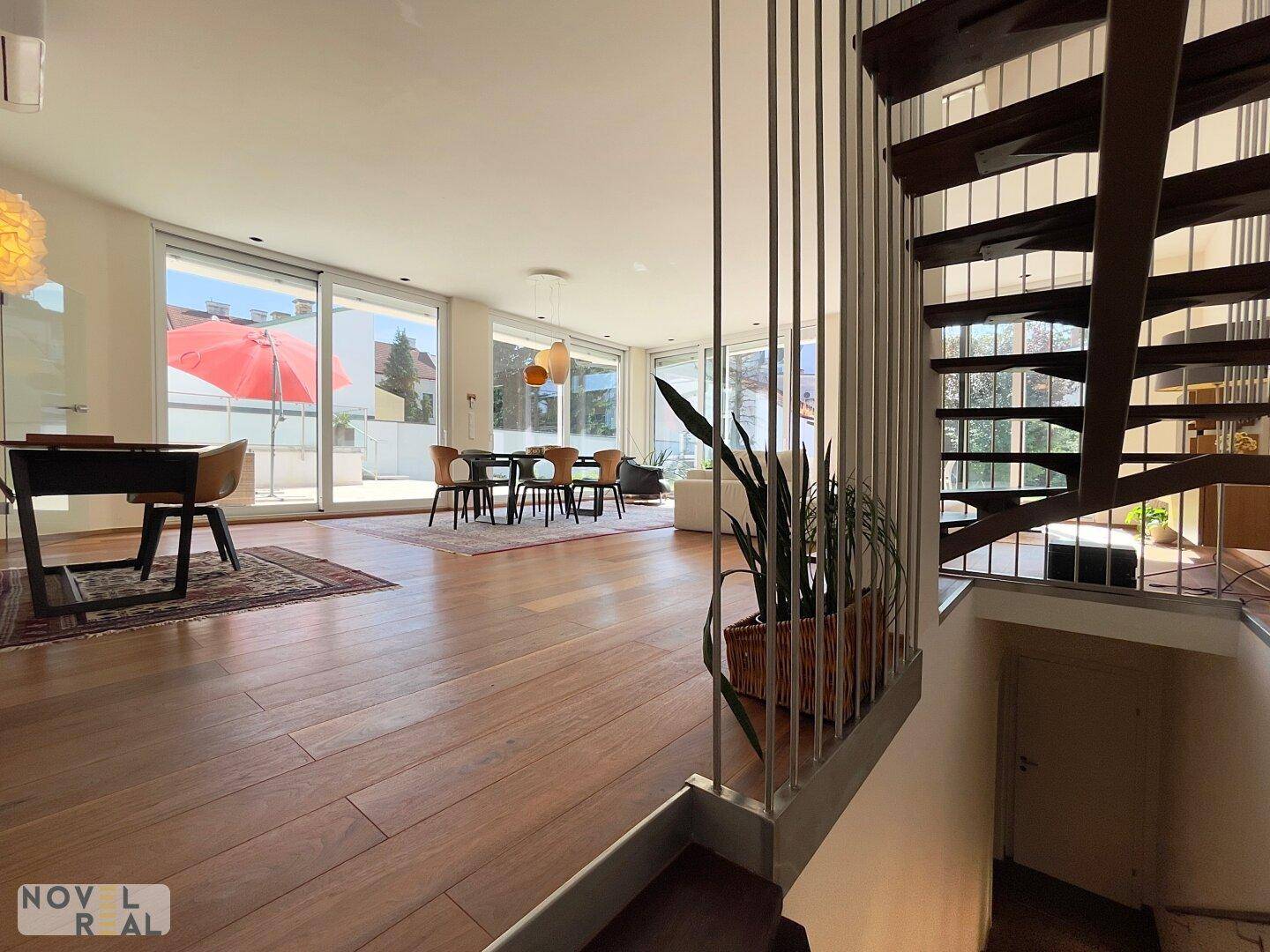 Lichtdurchfluteter Wohn-Essbereich mit Holzboden, Zugang zur Terrasse und eleganter Treppenkonstruktion.