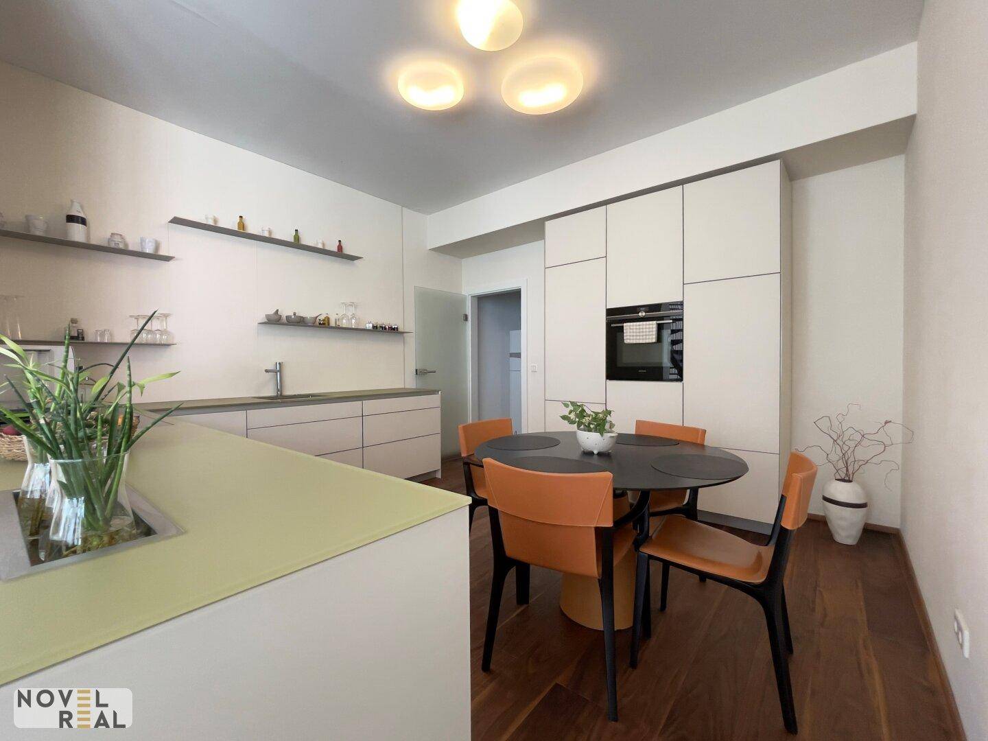 Moderne Küche mit heller Einbauküche, Kücheninsel und kleinem Essbereich.