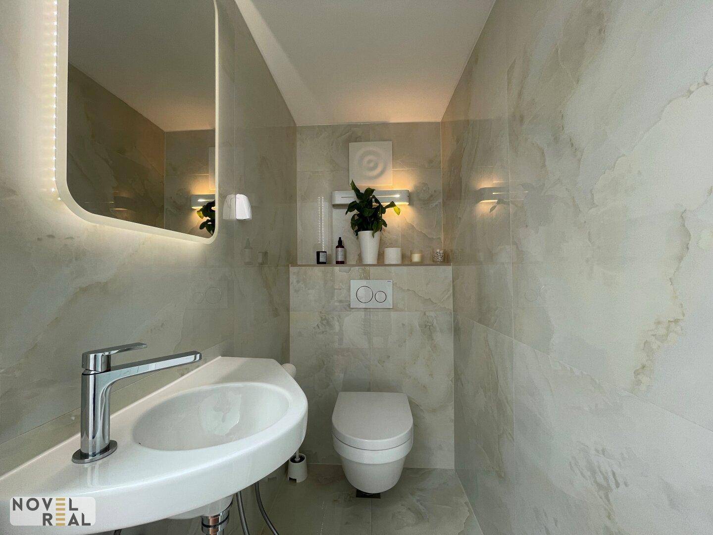 Modernes Gäste-WC mit Wand-WC, elegantem Waschbecken und großformatigen Fliesen.