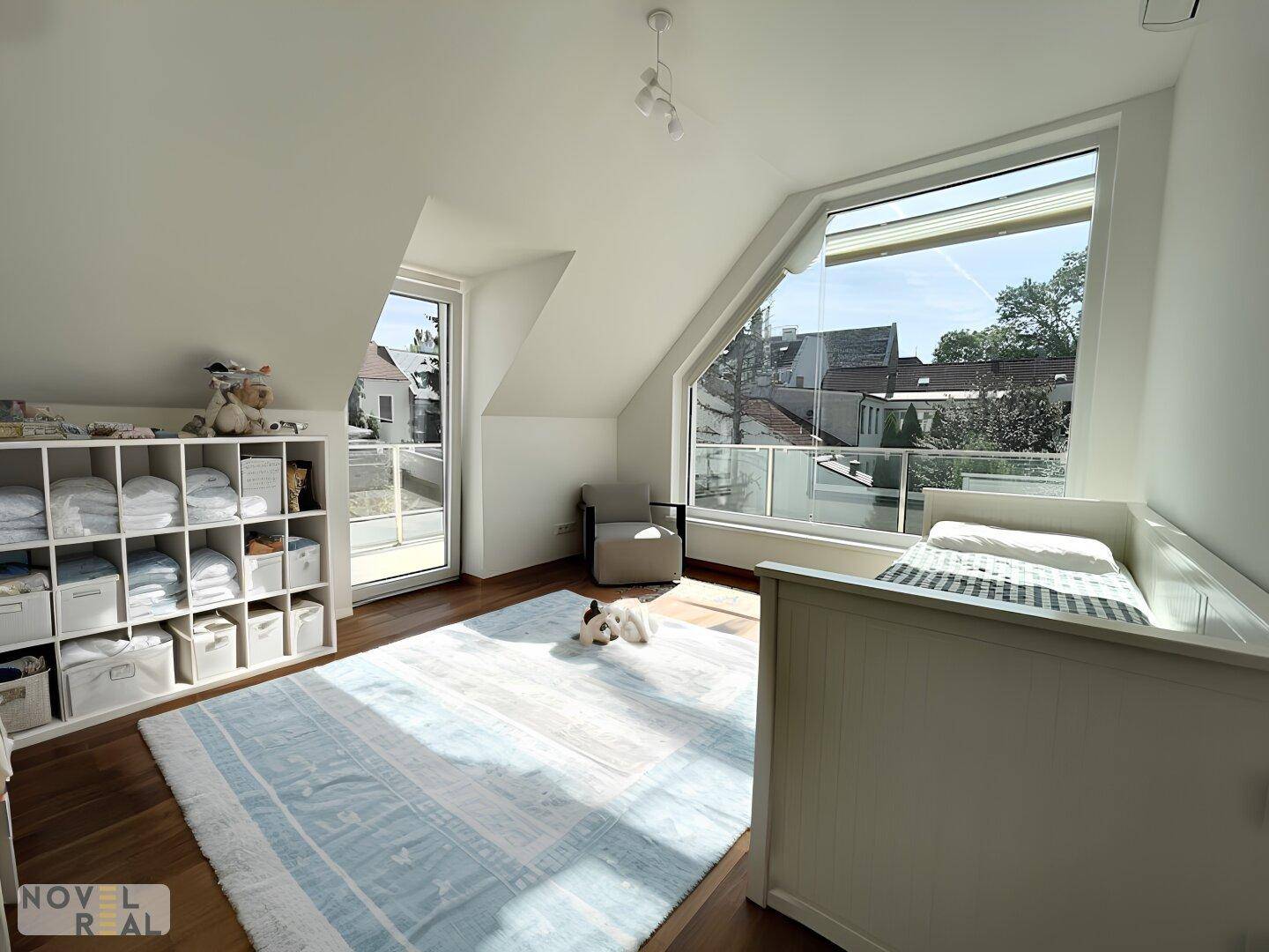 Helles Kinderzimmer mit Babybett, praktischen Regalen und einem großen, schrägen Fenster.