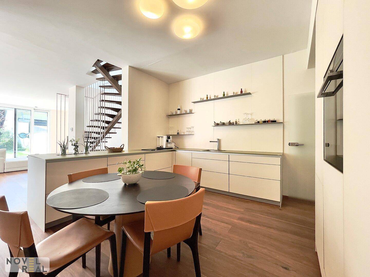 Moderne Küche mit Essbereich, weißen Schränken und Blick auf die offene Treppenkonstruktion.