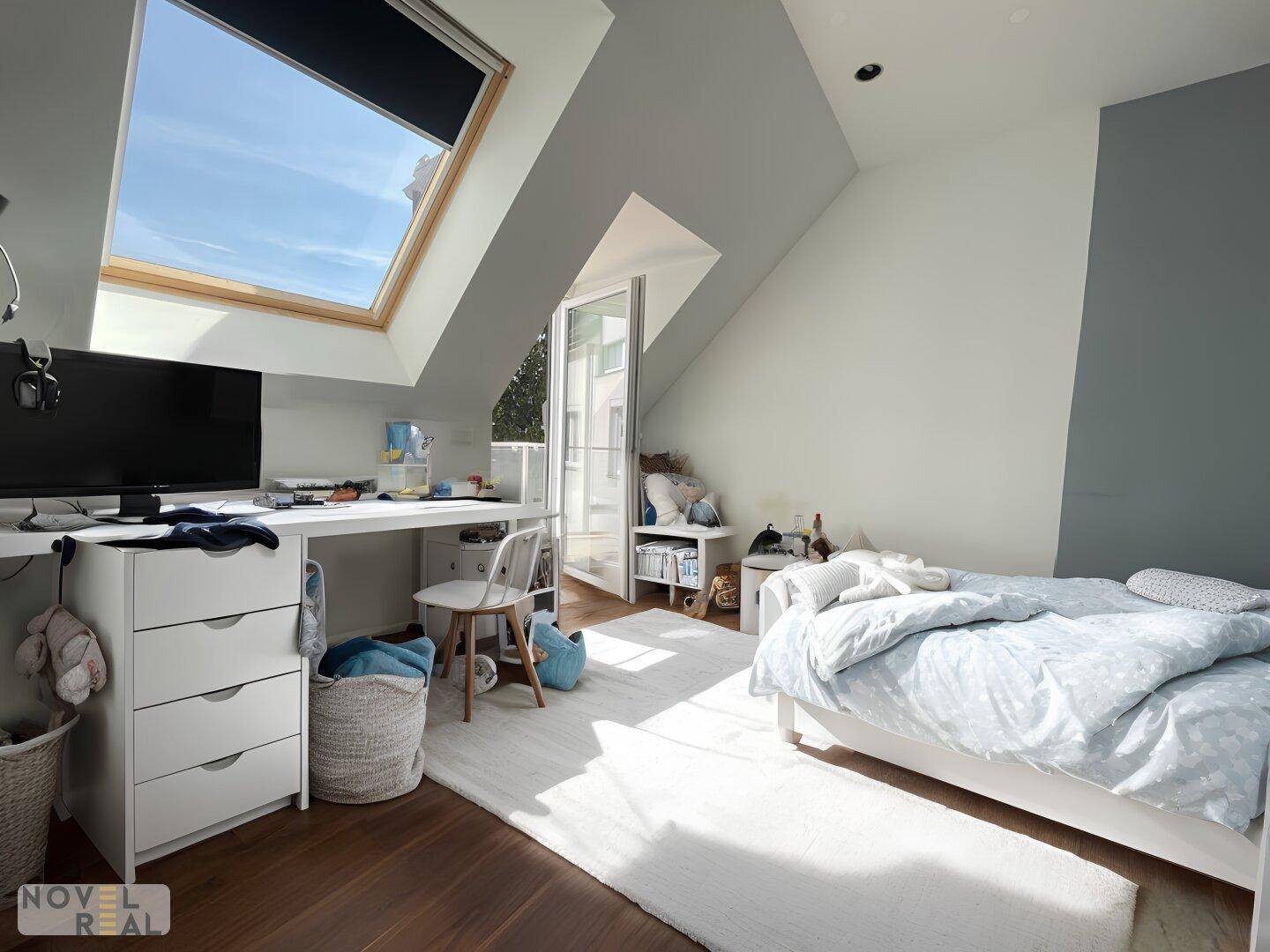 Helles Schlafzimmer im Dachgeschoss mit Dachfenster, Schreibtisch und Zugang zu einem kleinen Balkon.