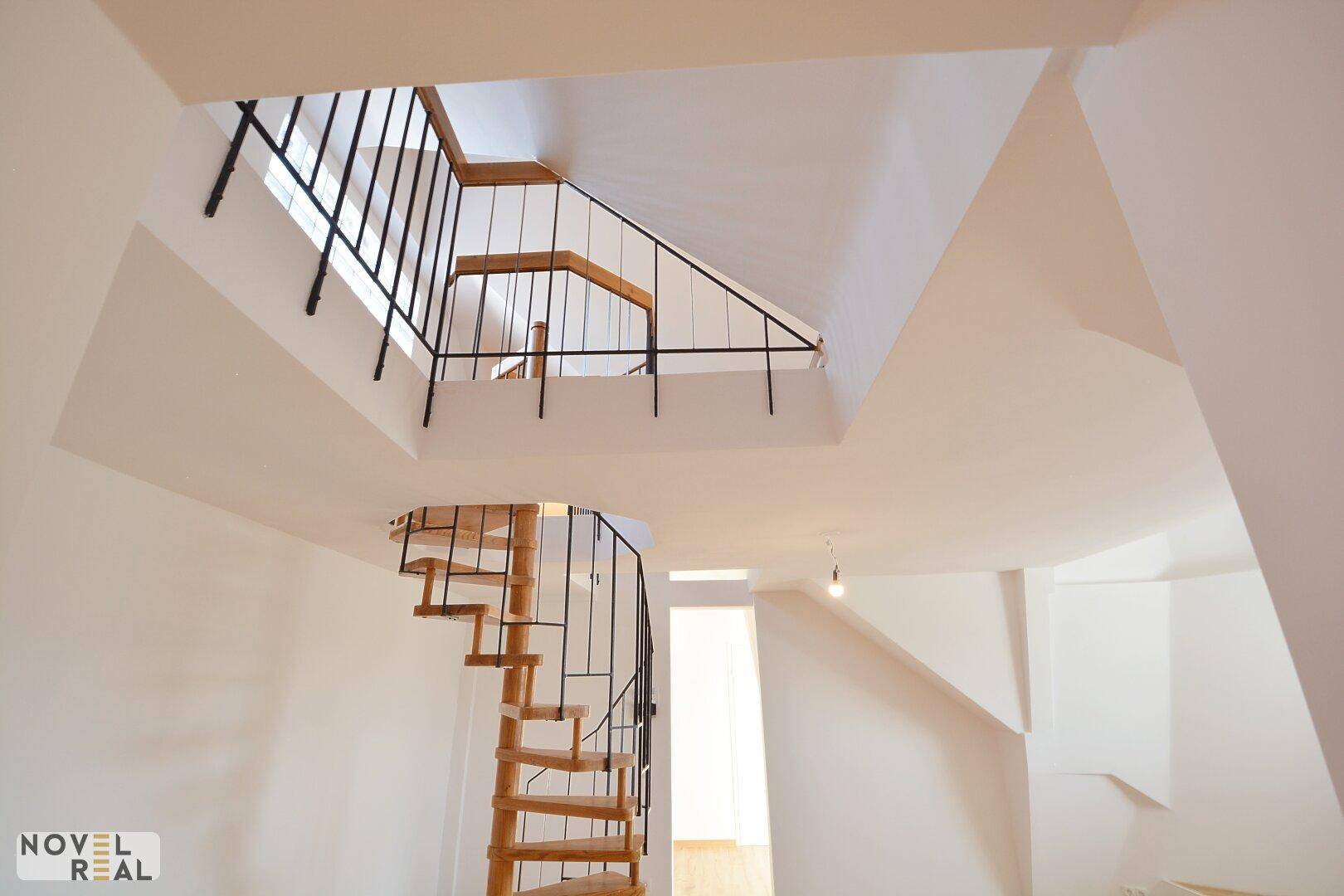 Ansicht der Holz-Wendeltreppe von unten, umgeben von hellen Wänden und schrägen Decken.