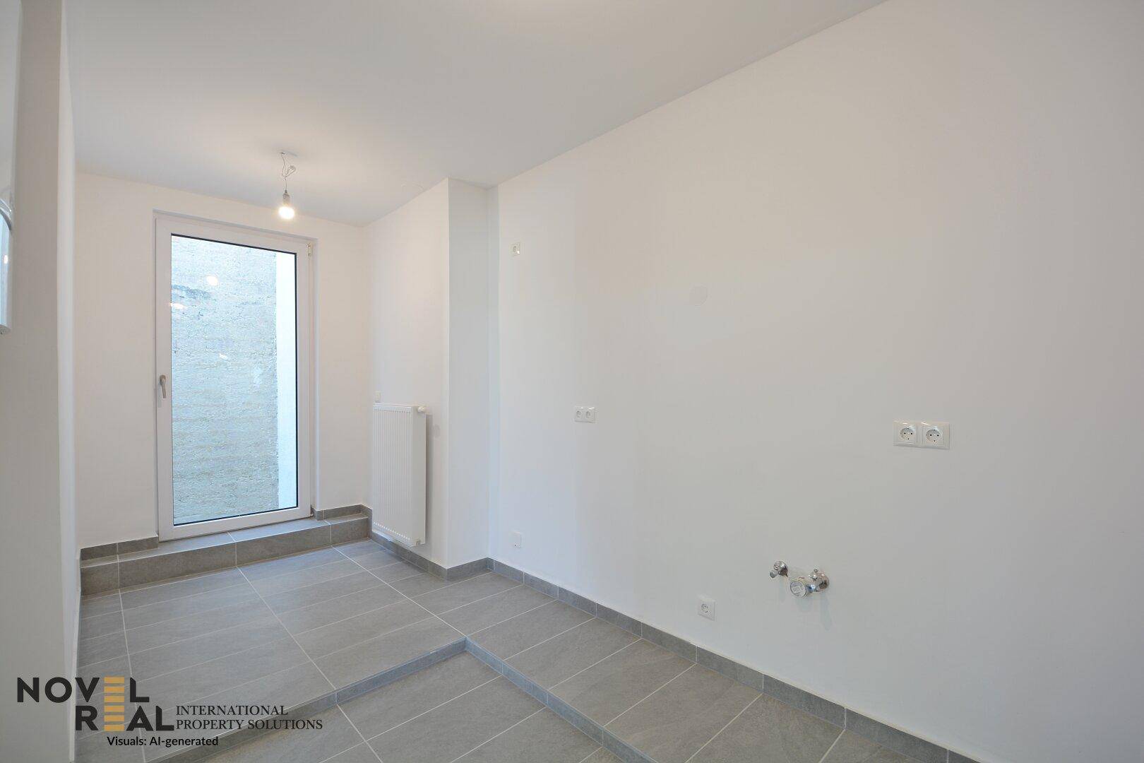 Leerer Raum mit grauen Fliesen, einem Fenster und Anschlüssen für eine mögliche Küchen- oder Waschküchennutzung.