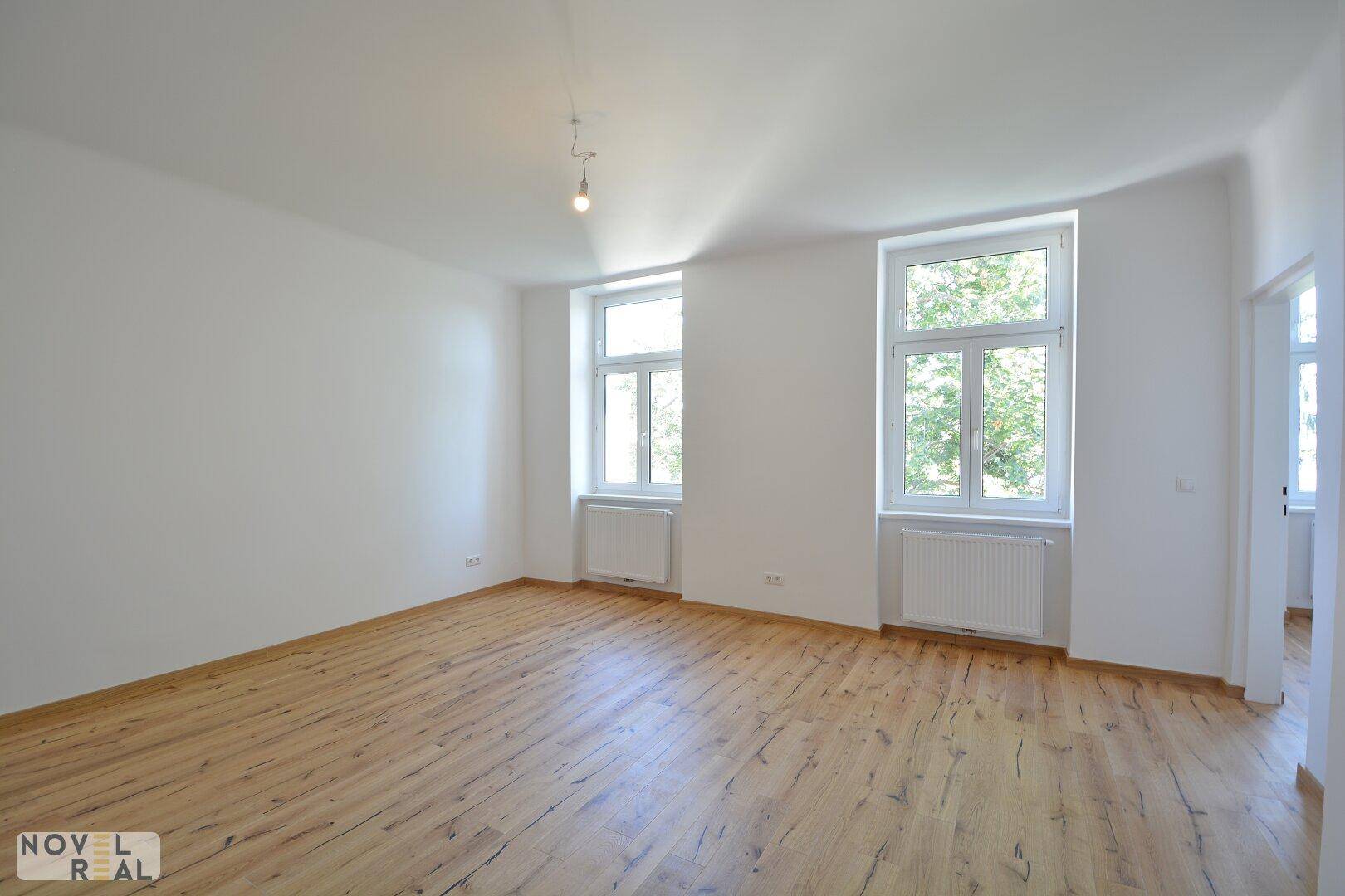 Geräumiges Wohnzimmer mit Holzboden und großen Fenstern, bietet viel Gestaltungspotenzial.