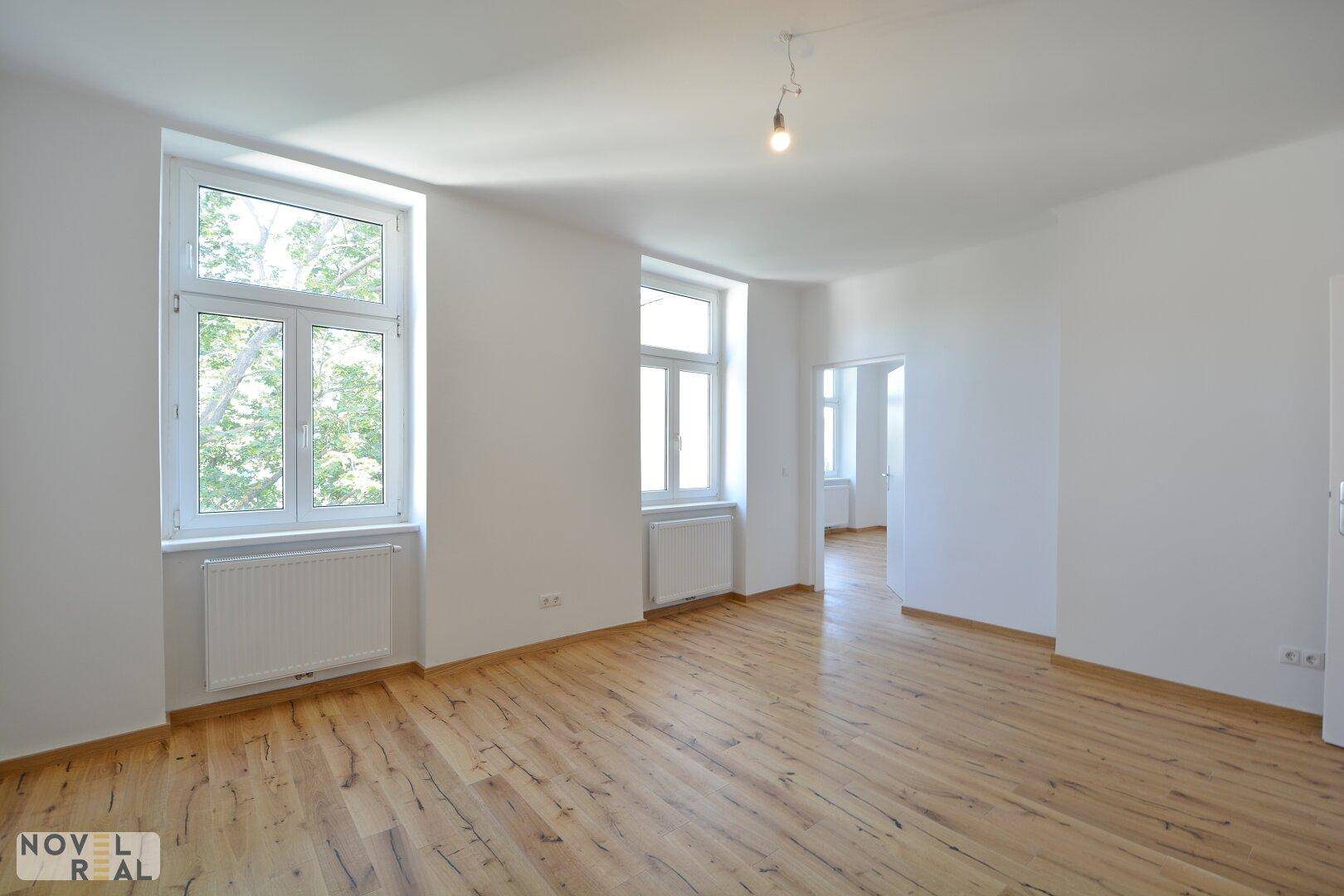 Helles und leeres Wohnzimmer mit Holzboden und mehreren Fenstern, bereit zum Einrichten.