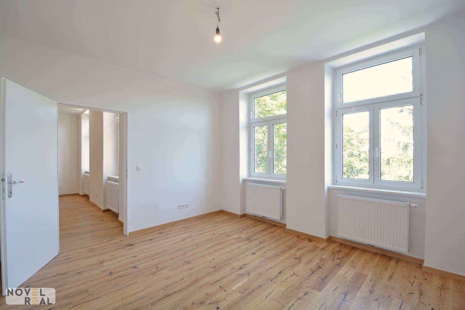 Leeres Schlafzimmer mit Holzboden und großen Fenstern, bietet eine helle und ruhige Atmosphäre.