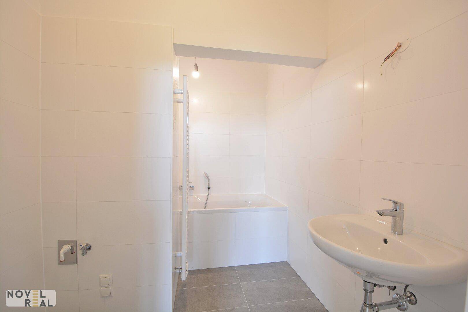 Modern gefliestes Badezimmer mit Badewanne und Waschbecken, in hellen Farbtönen gehalten.