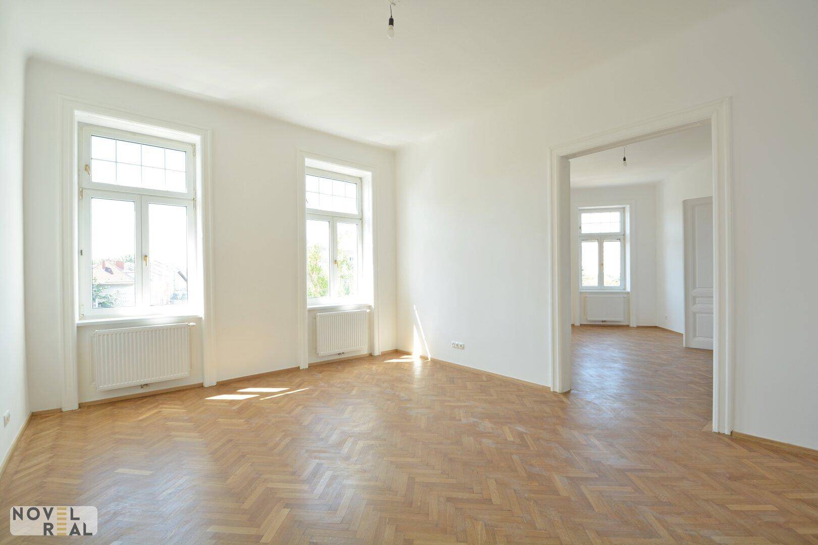 Großzügiger, heller Raum mit Fischgrätparkett und vielen Fenstern, ideal für Wohnzwecke.