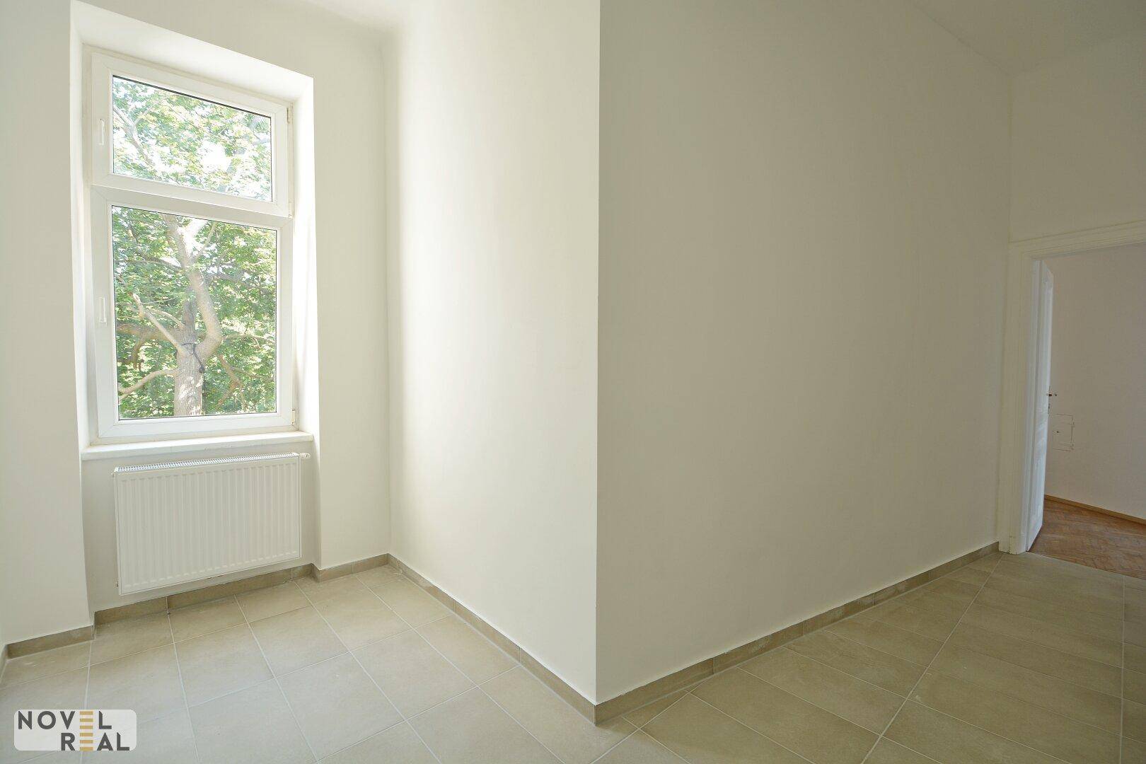 Kleiner, heller Raum mit Fliesenboden und einem Fenster mit Blick ins Grüne.