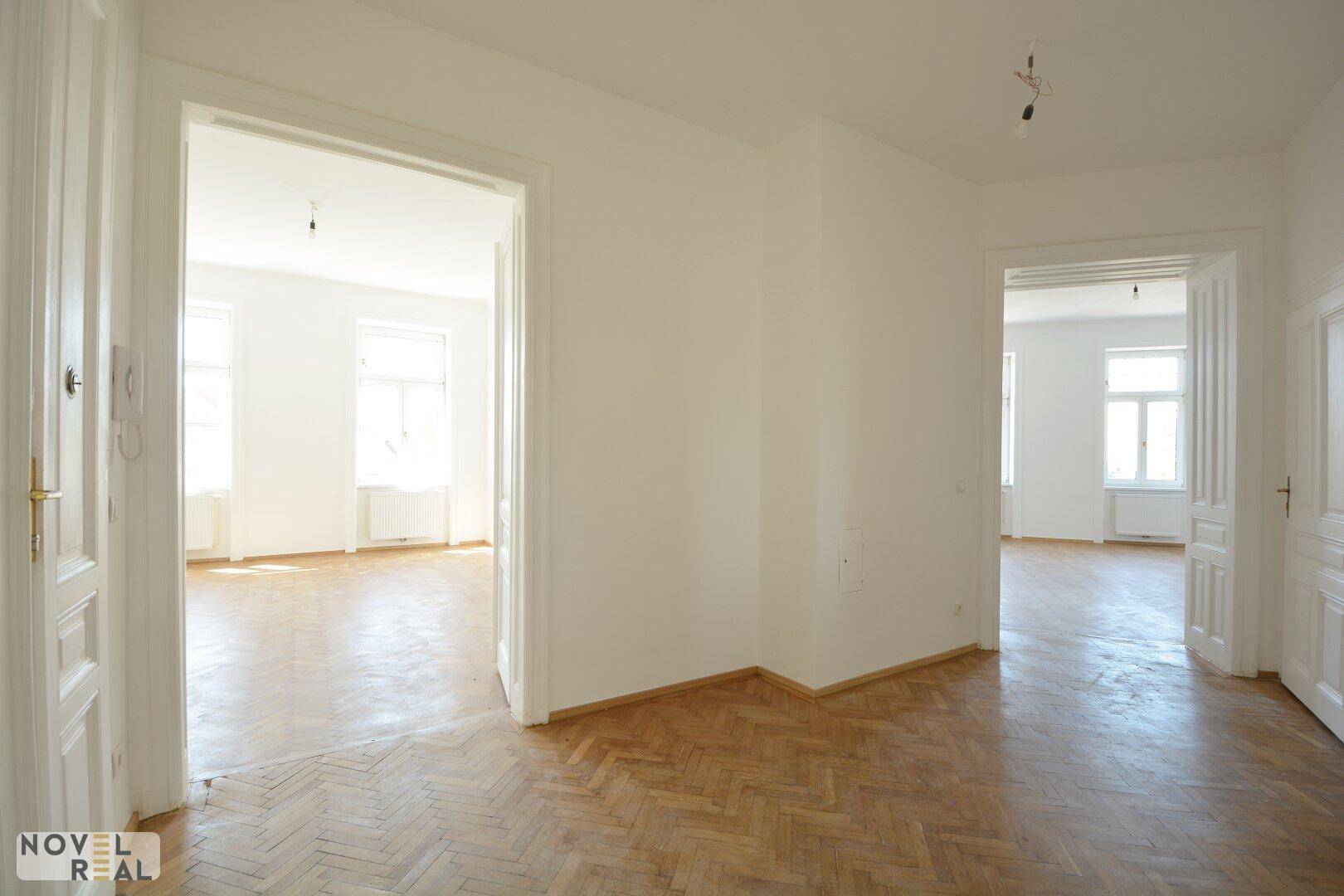 Heller Raum mit Fischgrätparkett und hohen Türen, der mehrere Zimmer verbindet.