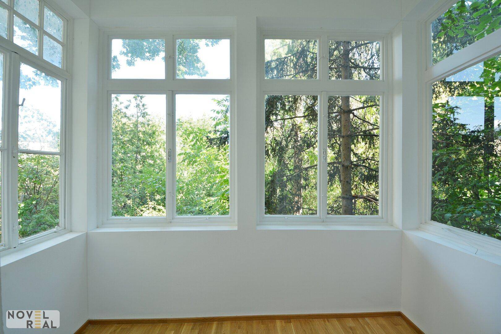 Heller Wintergarten mit vielen Fenstern, die einen direkten Blick auf grüne Bäume bieten.