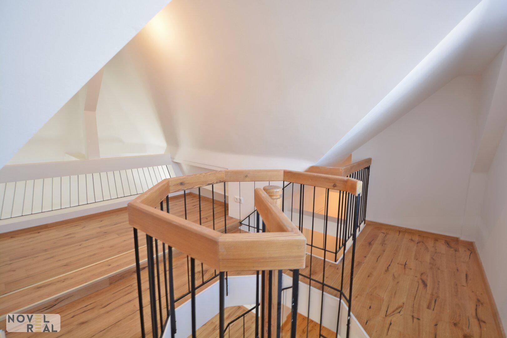 Blick auf eine elegante Holz-Wendeltreppe mit schwarzem Geländer und Laminatboden im Dachgeschoss.