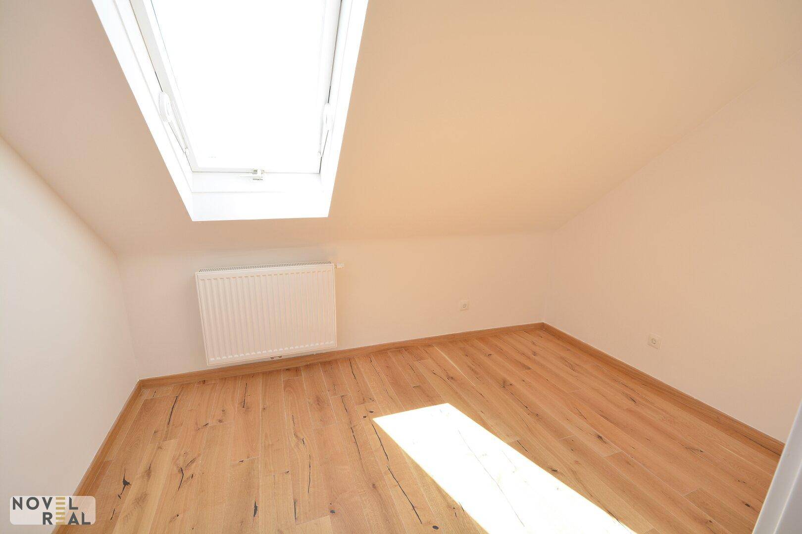 Helles Schlafzimmer mit Holzboden, Dachschräge und einem großen Dachfenster, das viel Licht spendet.