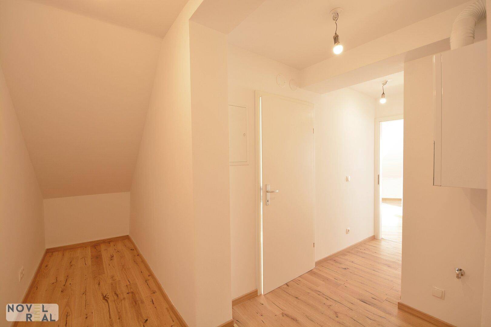 Heller Flur mit Holzfußboden und einer Nische unter der Dachschräge, ideal als Abstellraum.