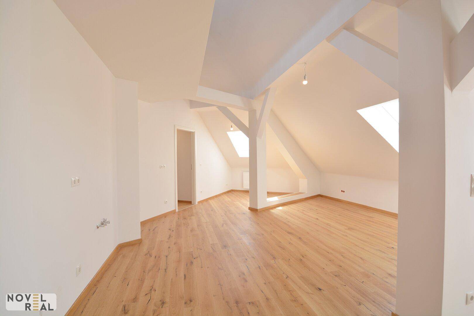 Großzügiger, heller Raum mit Holzboden, Dachschrägen und sichtbaren Holzbalken, bereit zur individuellen Gestaltung.
