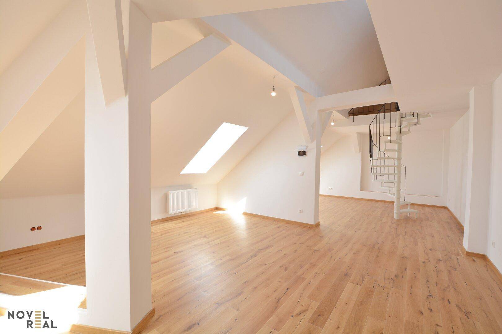 Geräumiger, heller Wohnbereich mit Dachschrägen, Holzboden und einer Wendeltreppe, die zum oberen Stockwerk führt.