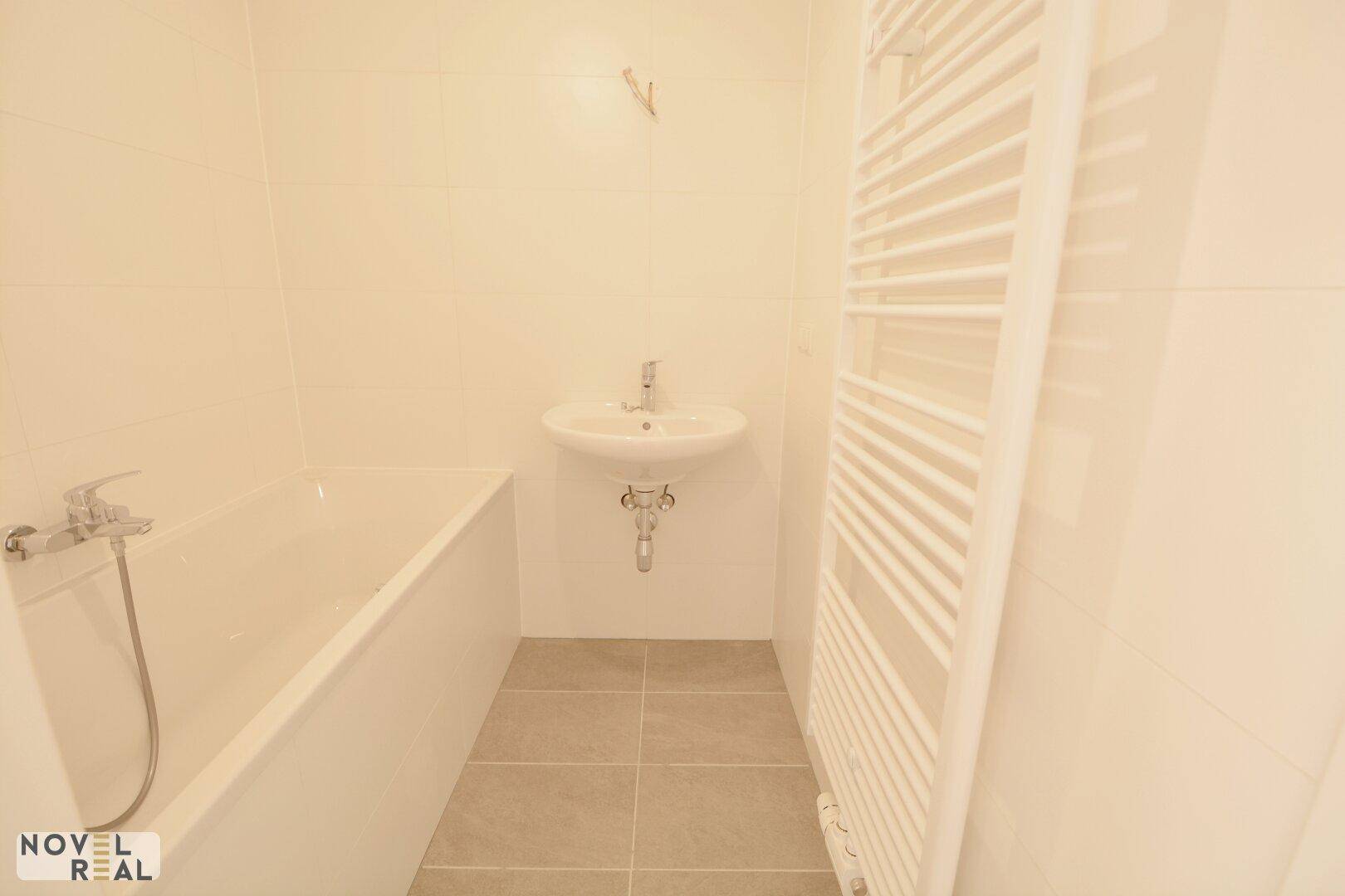 Helles Badezimmer mit Badewanne, Waschbecken und beheiztem Handtuchhalter, modern gefliest.
