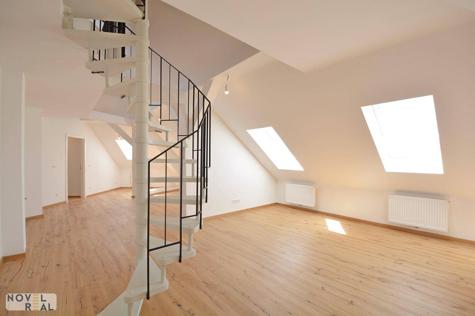 Heller Dachgeschossraum mit Wendeltreppe, Dachschrägen und viel Tageslicht durch die Dachfenster.