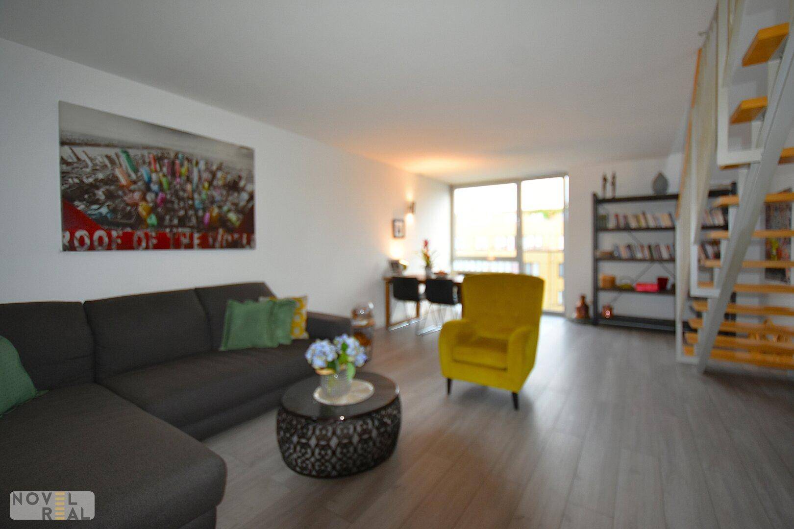 Heller Wohn- und Essbereich mit großem Sofa, gelbem Sessel und Zugang zu einem Balkon.
