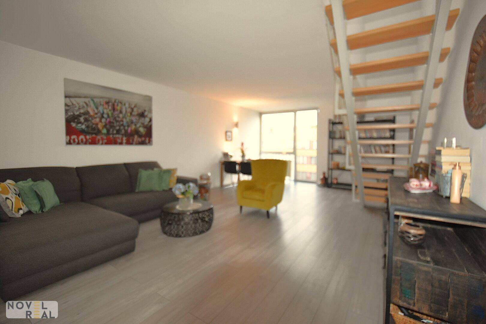 Großzügiges Wohnzimmer mit bequemer Sitzecke, gelbem Akzentsessel und offener Treppe.