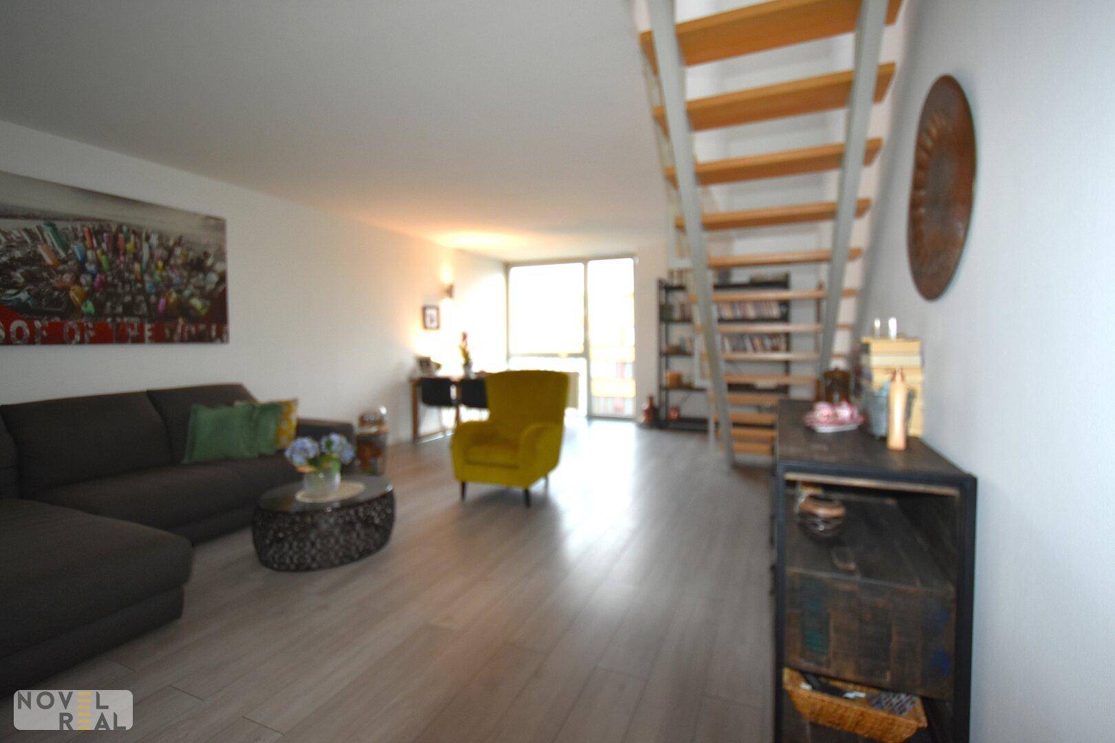Geräumiger Wohn-Essbereich mit Sofa, Esstisch und offener Treppe, hell und modern eingerichtet.