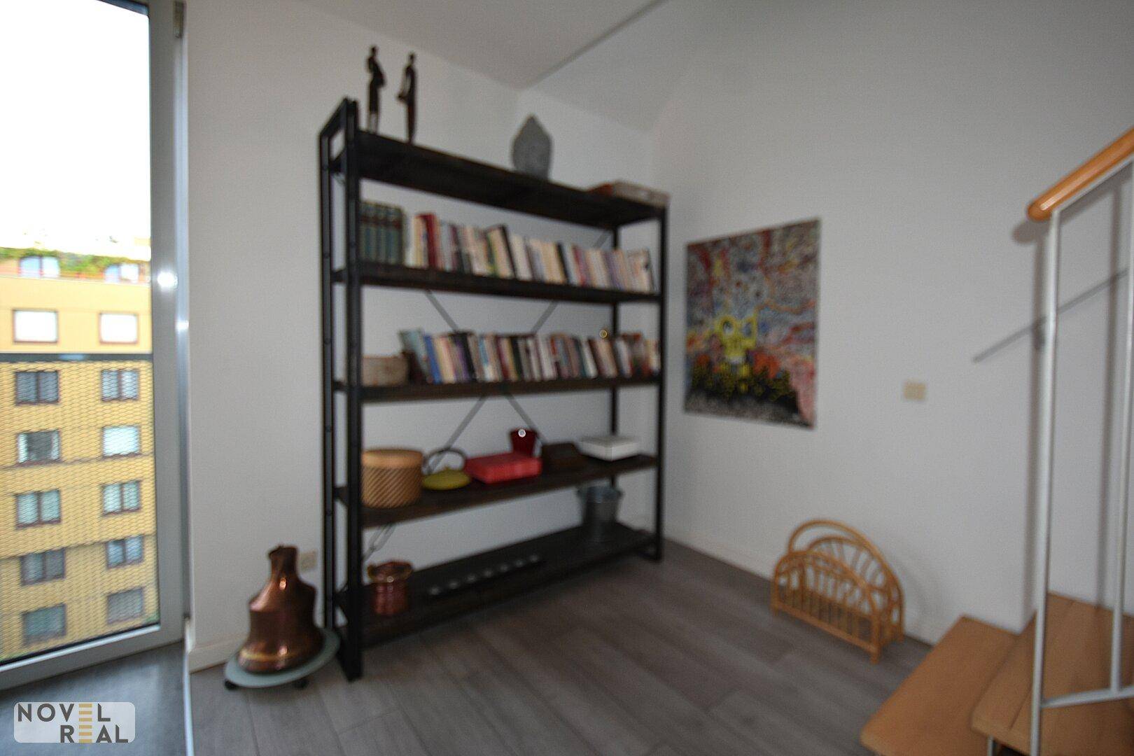 Heller Bereich mit Bücherregal und großem Fenster, ideal als Leseecke oder Arbeitsplatz.