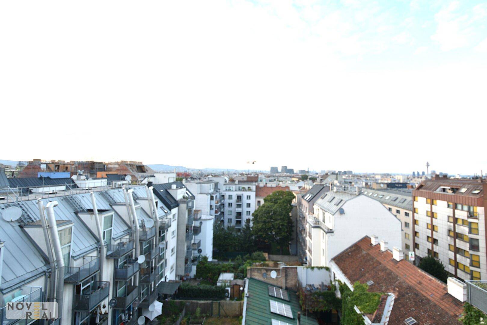 Weitläufiger Blick über die Dächer der Stadt mit Wohngebäuden und Grünflächen.