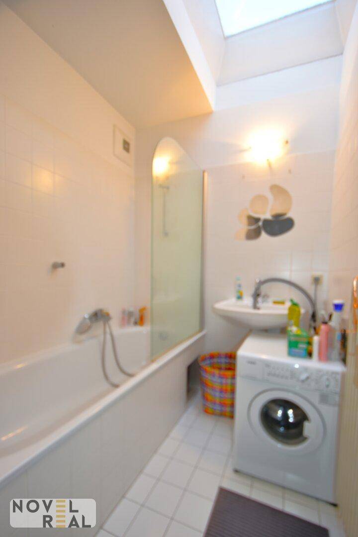 Helles Badezimmer mit Badewanne, Waschbecken, Waschmaschine und Dachfenster.