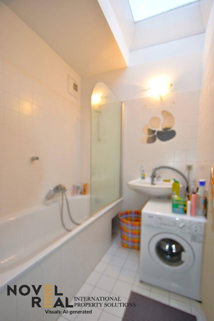 Helles Badezimmer mit Badewanne, Waschbecken, Waschmaschine und Dachfenster.