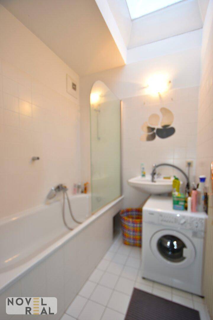 Helles Badezimmer mit Badewanne, Waschbecken, Waschmaschine und Dachfenster.