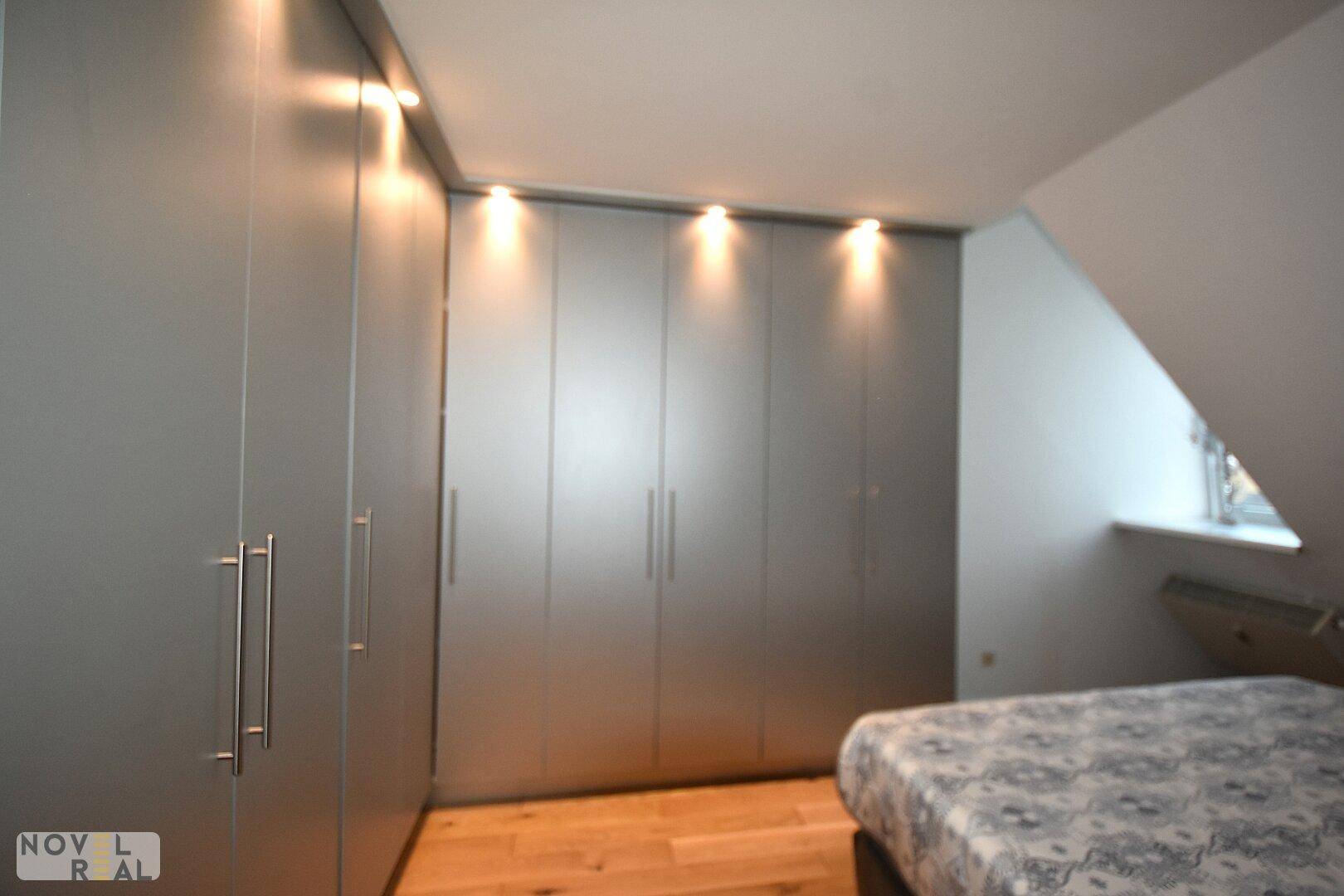 Schlafzimmer mit modernen Einbauschränken, Holzboden und schräger Decke.