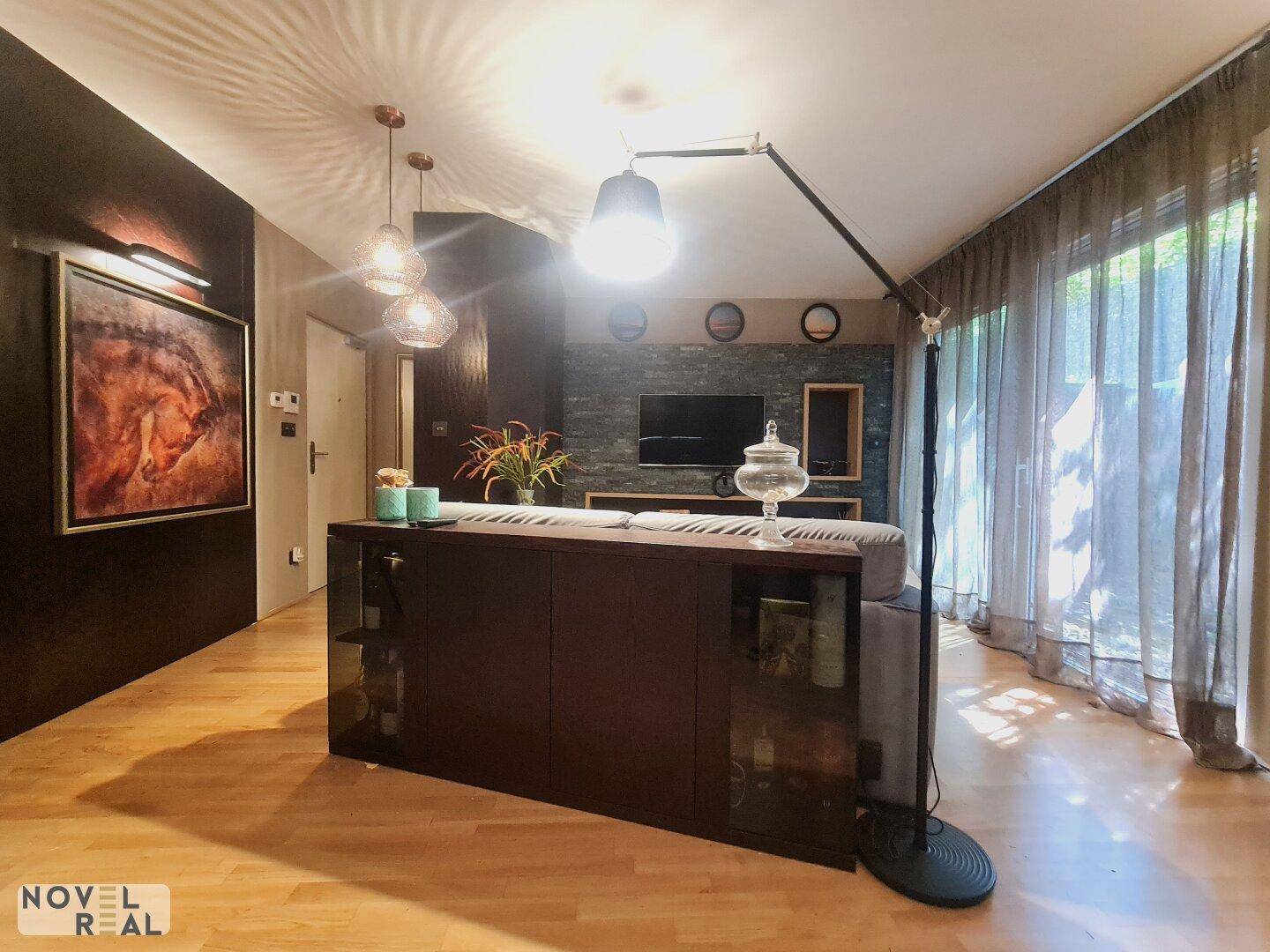 Detailansicht des Wohnzimmers mit bequemer Couch, Stehlampe und Zugang zur Terrasse.