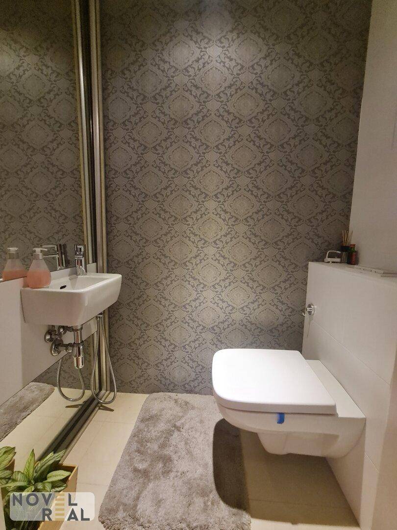 Gäste-WC mit wandhängender Toilette, kleinem Waschbecken und gemusterter Tapete.