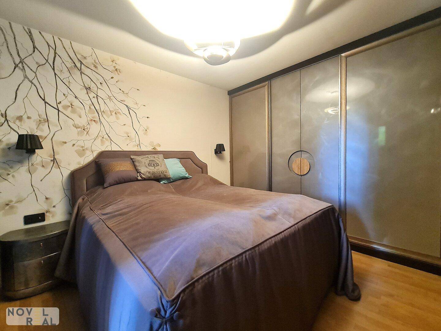 Helles Schlafzimmer mit Holzboden, dekorativer Tapete und geräumigen Einbauschränken.