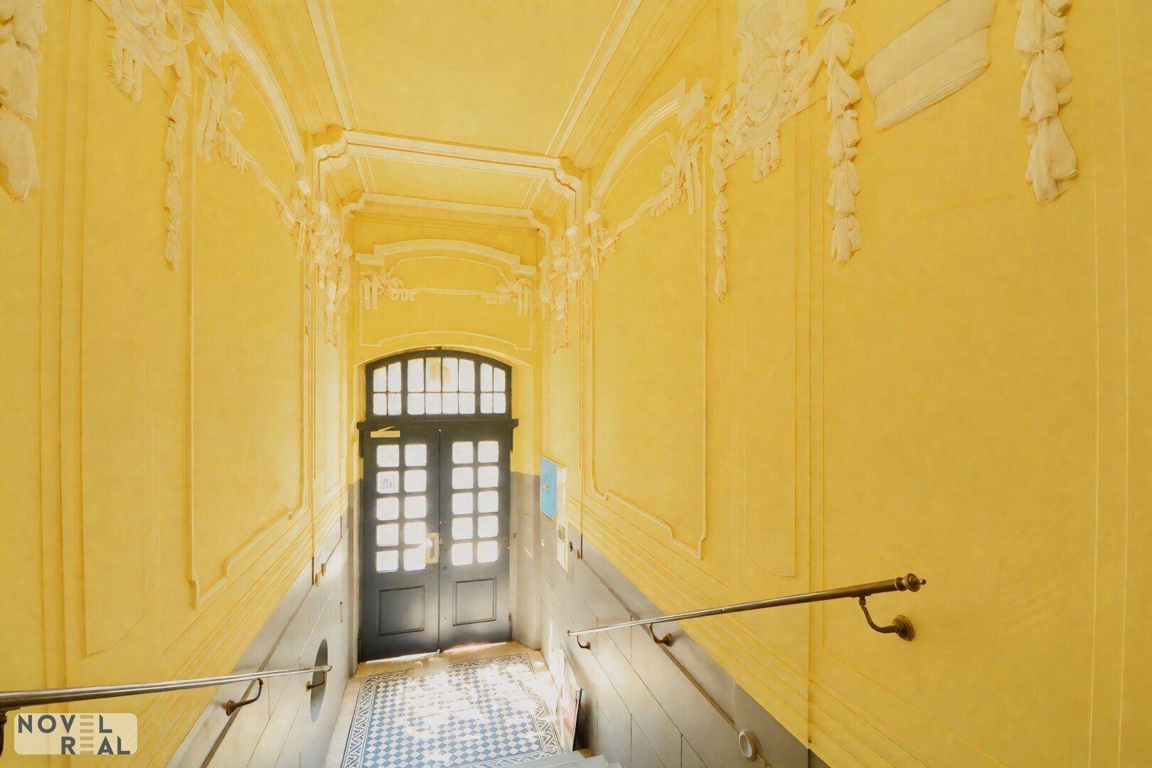 Historischer Hausflur mit aufwendigen Stuckverzierungen, gelben Wänden und gemusterten Fliesen.