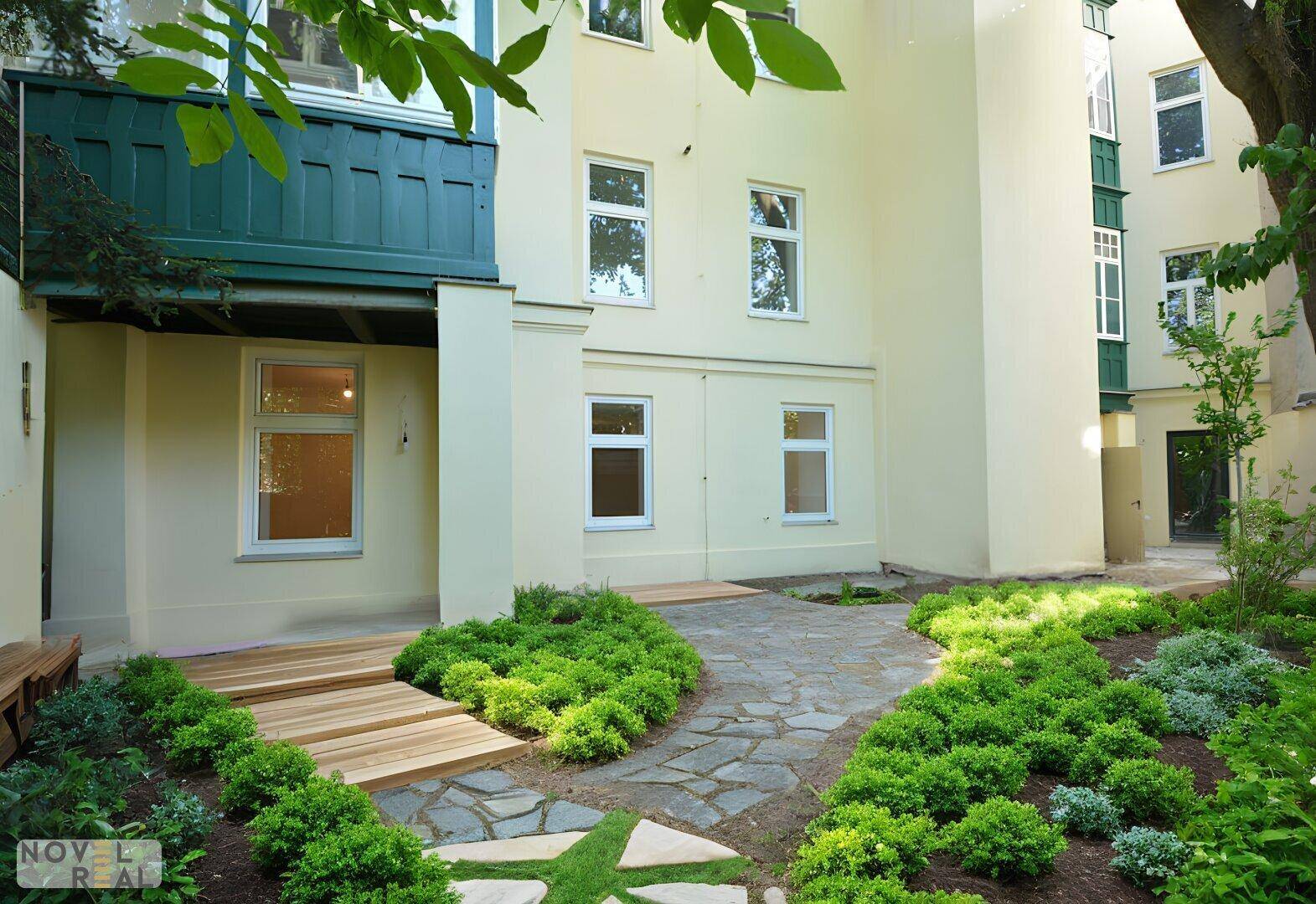 Gepflegter Gartenbereich mit Steinweg und Holzterrasse vor der hellen Fassade des Gebäudes.