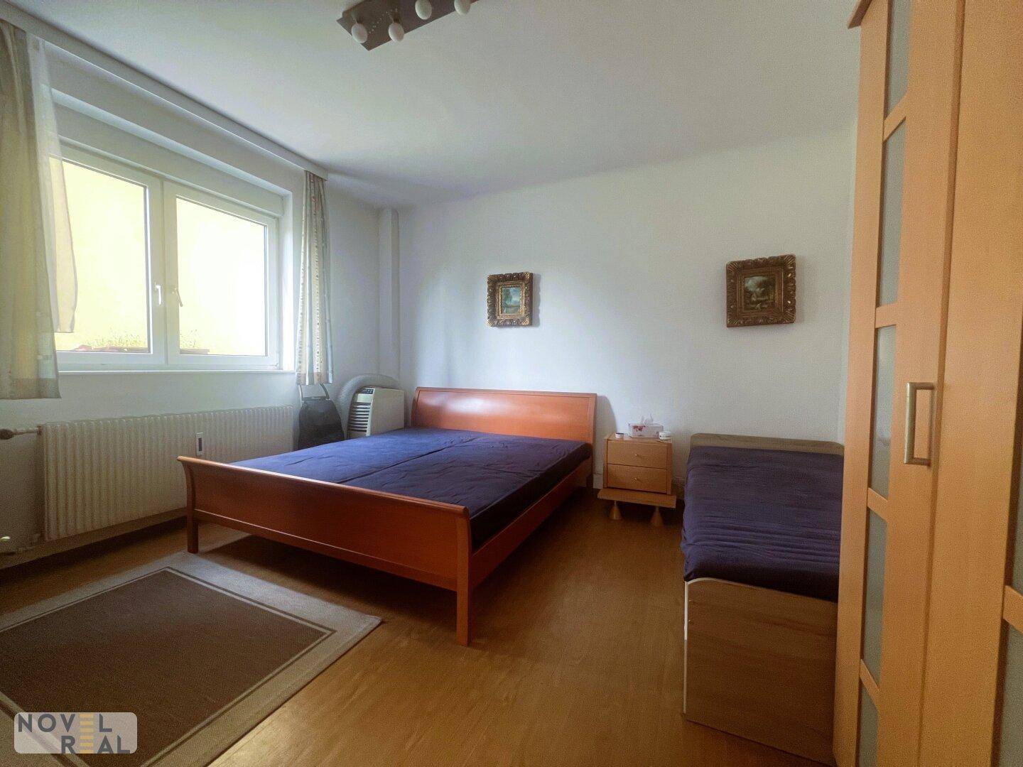 Gemütliches Schlafzimmer mit Doppelbett, Parkettboden und Fenster, dekoriert mit Bildern.