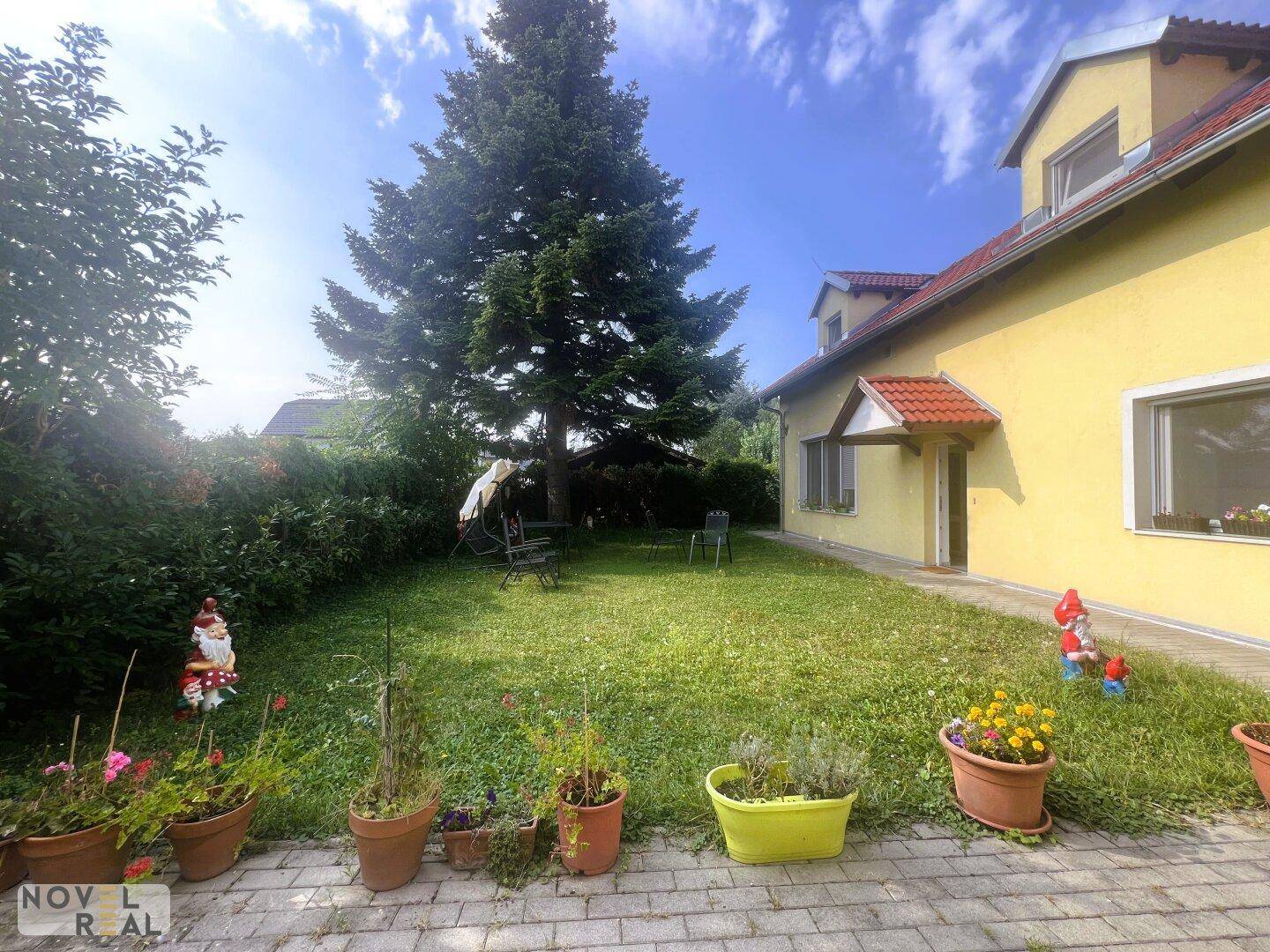 Großer Gartenbereich mit altem Baum, Blumenkübeln und Gartenfiguren, ideal zum Entspannen.