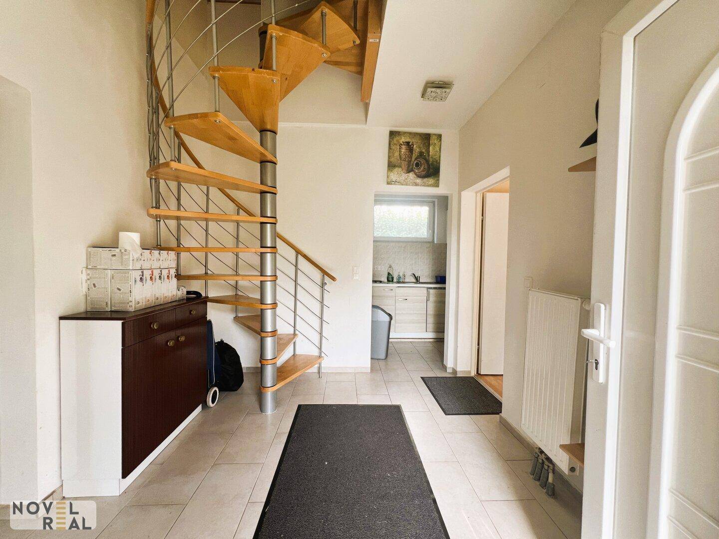 Heller Flur mit einer eleganten Wendeltreppe und Zugang zu einer kleinen Küchenzeile.