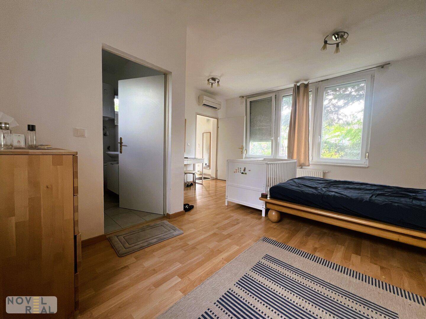 Schlafzimmer mit Holzboden und Blick in einen angrenzenden Raum, ausgestattet mit Klimaanlage.