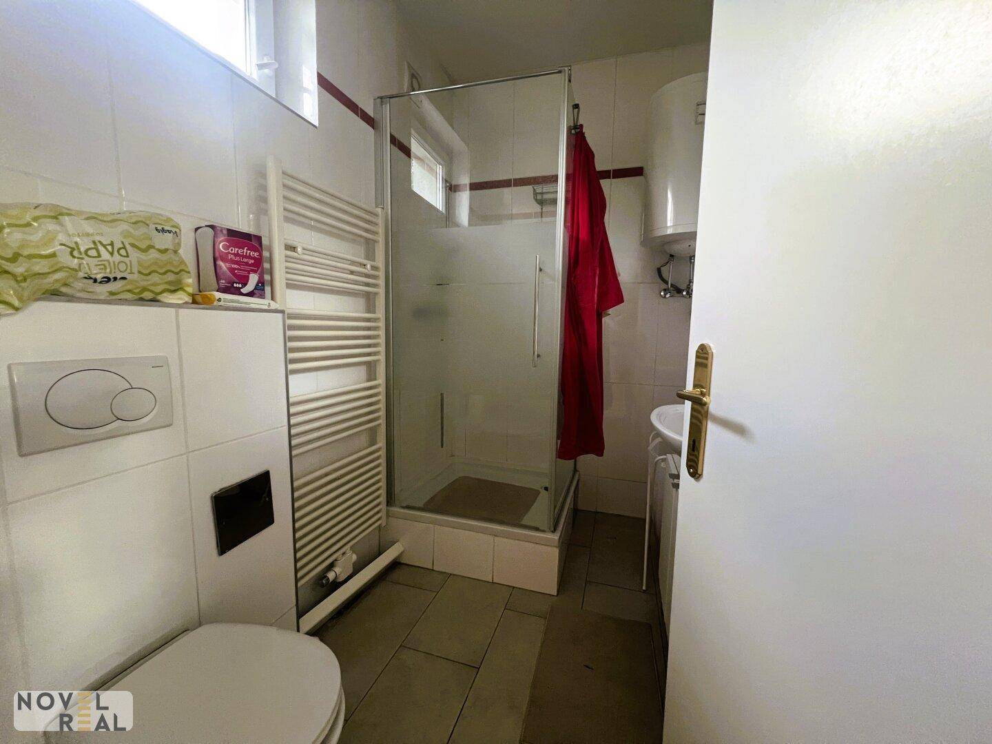 Funktionales Badezimmer mit Toilette, Duschkabine und Handtuchheizkörper, hell gefliest.