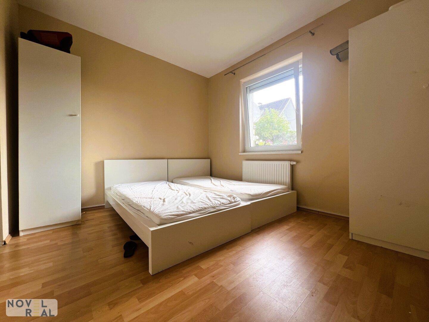Helles Schlafzimmer mit zwei Einzelbetten, Parkettboden und großem Fenster, einfach eingerichtet.