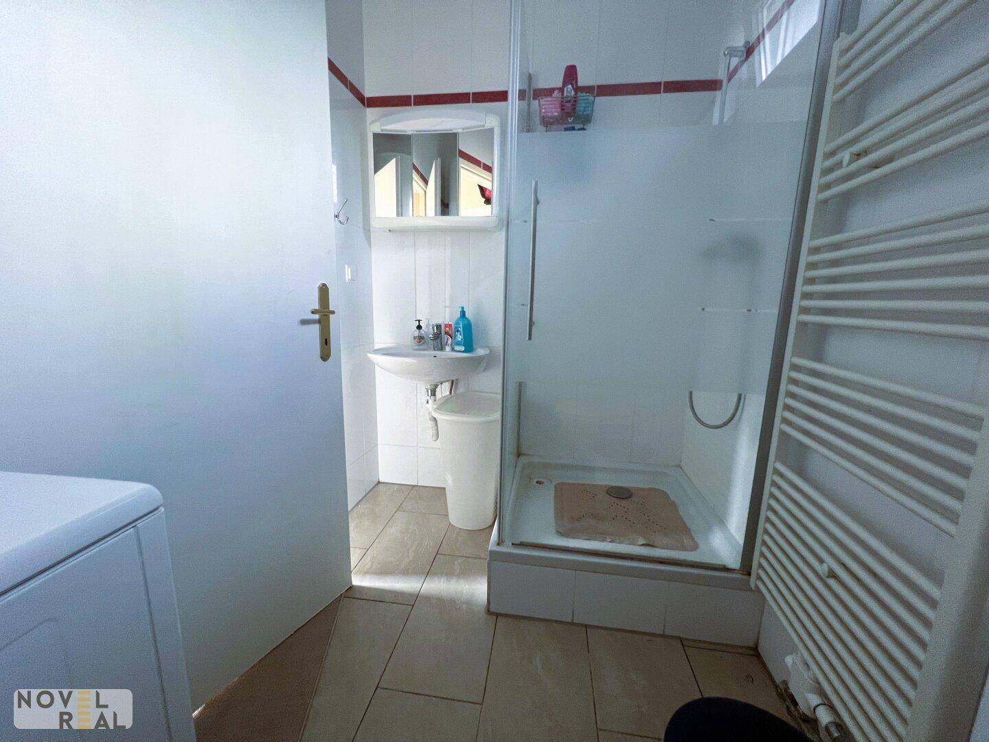 Badezimmer mit Duschkabine, Waschbecken und Fliesenboden, ausgestattet mit einem Handtuchheizkörper.