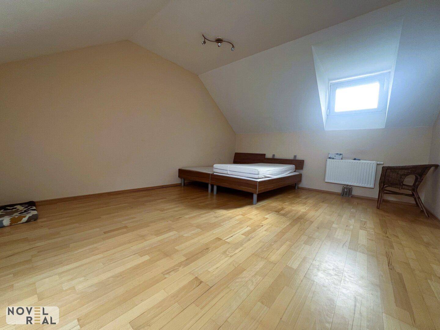 Helles Schlafzimmer im Dachgeschoss mit Holzboden, Dachschräge und einem Dachfenster.