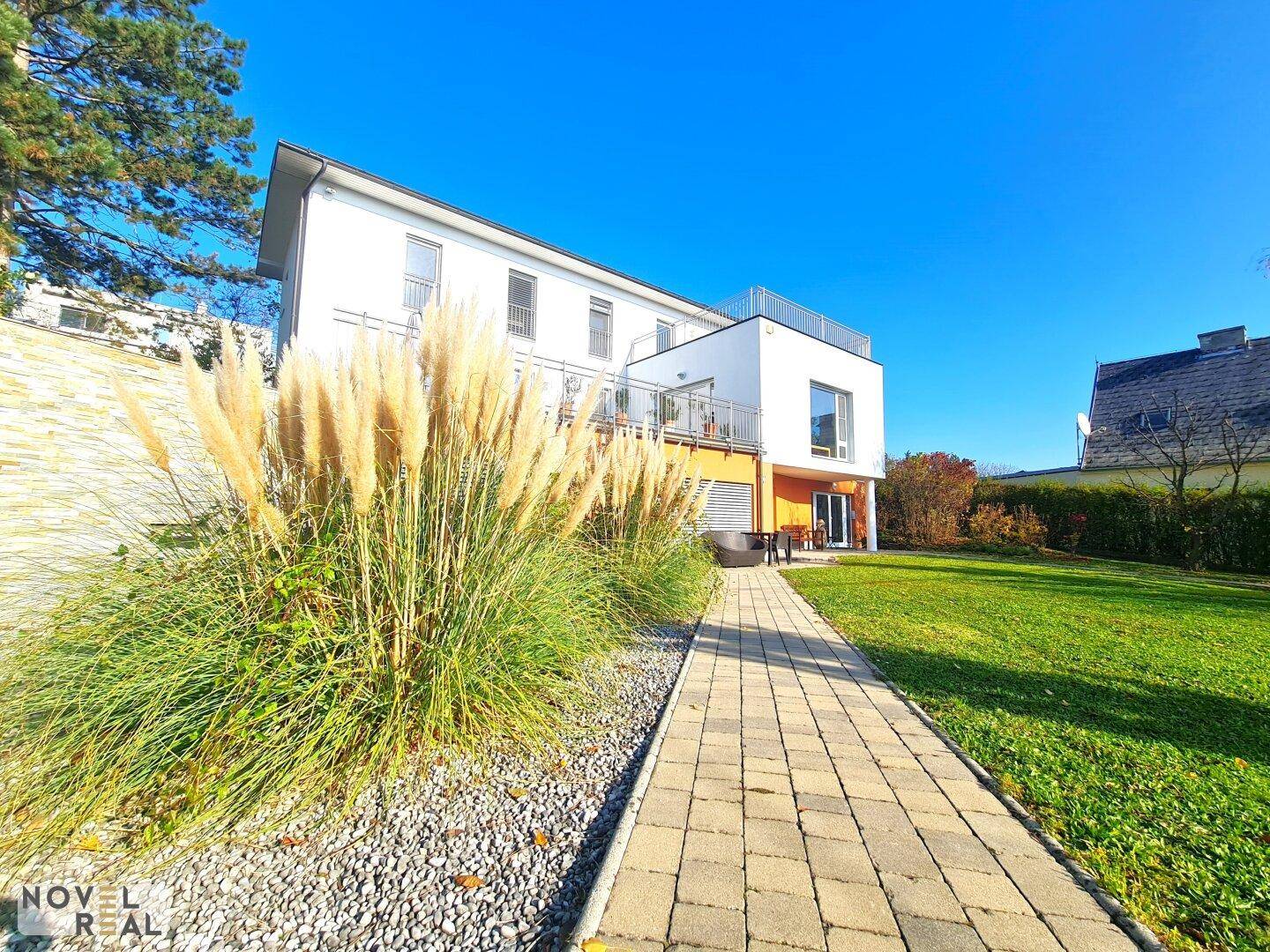 Gepflegter Garten mit Ziergräsern und gepflastertem Weg, der zum modernen Haus führt.