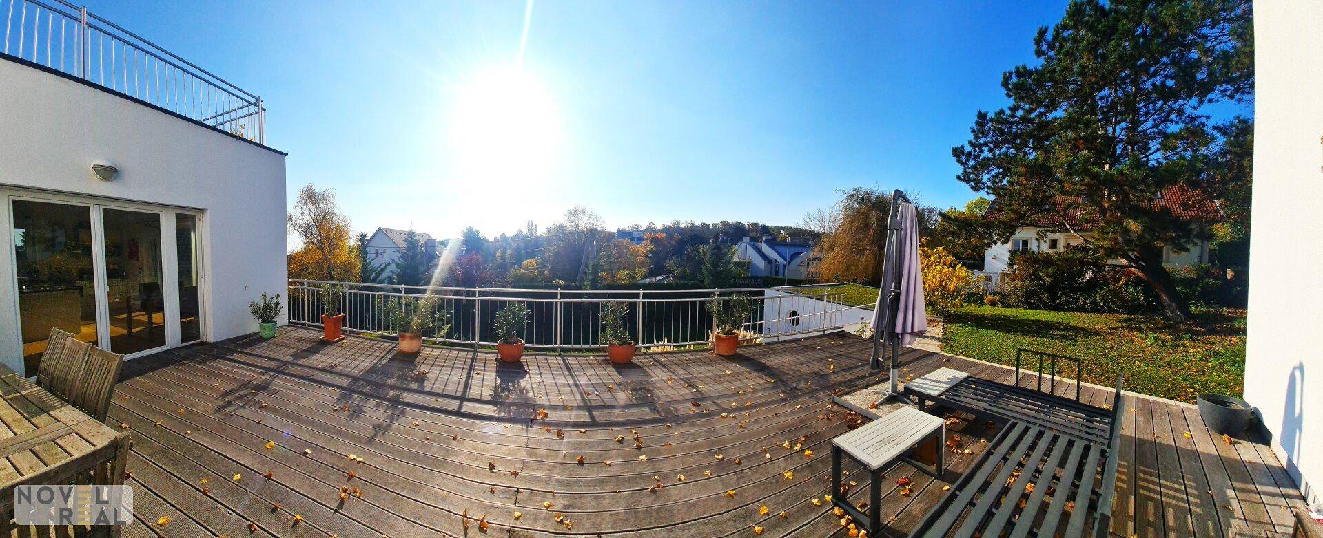 Große Holzterrasse mit Sitzgelegenheiten und weitem Blick über die Landschaft an einem sonnigen Tag.