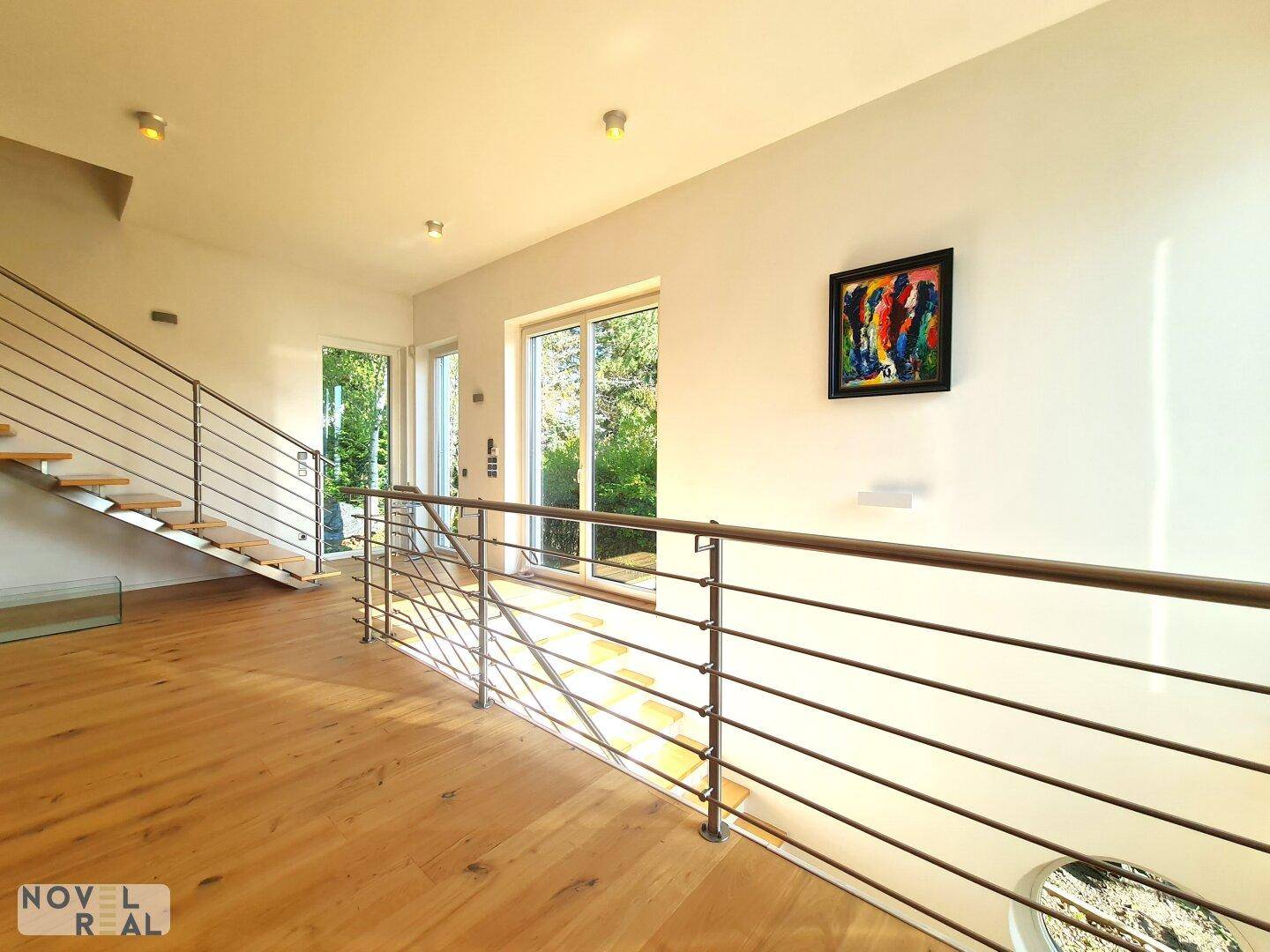 Heller Flurbereich mit moderner Treppe und großen Fenstern, die viel Licht hereinlassen.